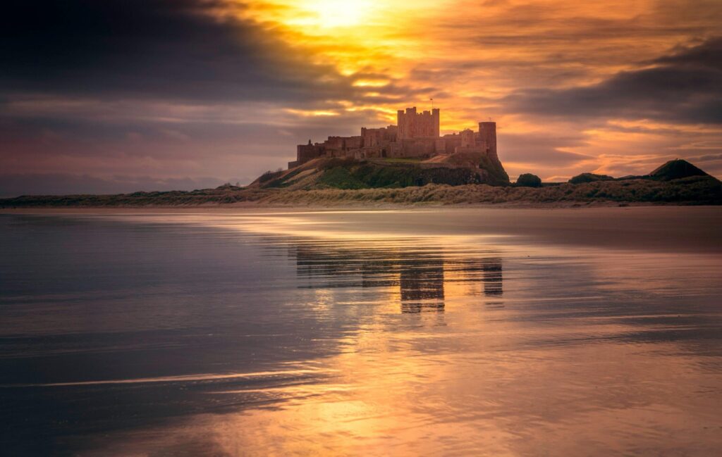 Stunning view of a castle reflecting on the tranquil beach at sunset, surrounded by a golden horizon.